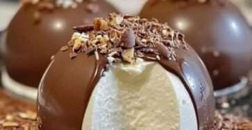 Dômes en chocolat brillants remplis de praliné et de mousse mascarpone, présentés sur une assiette élégante, avec une coque lisse et un intérieur crémeux.