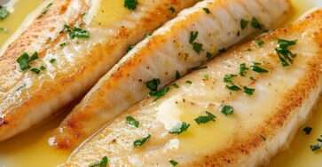 Filets de poisson blancs bien dorés, nappés d’un beurre citronné brillant, accompagnés de persil ciselé, présentés dans une assiette claire avec une sauce légère et onctueuse.