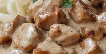 Sauté de porc à la moutarde dans une poêle, avec morceaux dorés, sauce crémeuse aux herbes de Provence et oignons fondants, prêt à être servi.